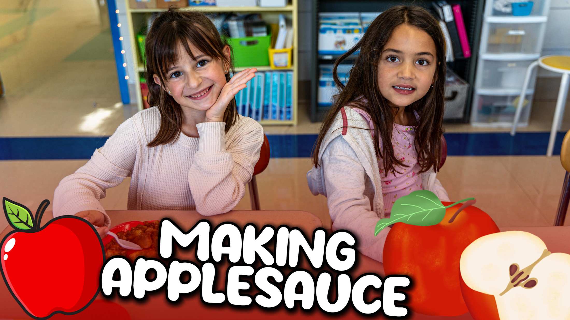 Two smiling elementary students sit at a table with bowls of homemade applesauce, participating in a classroom activity decorated with apple